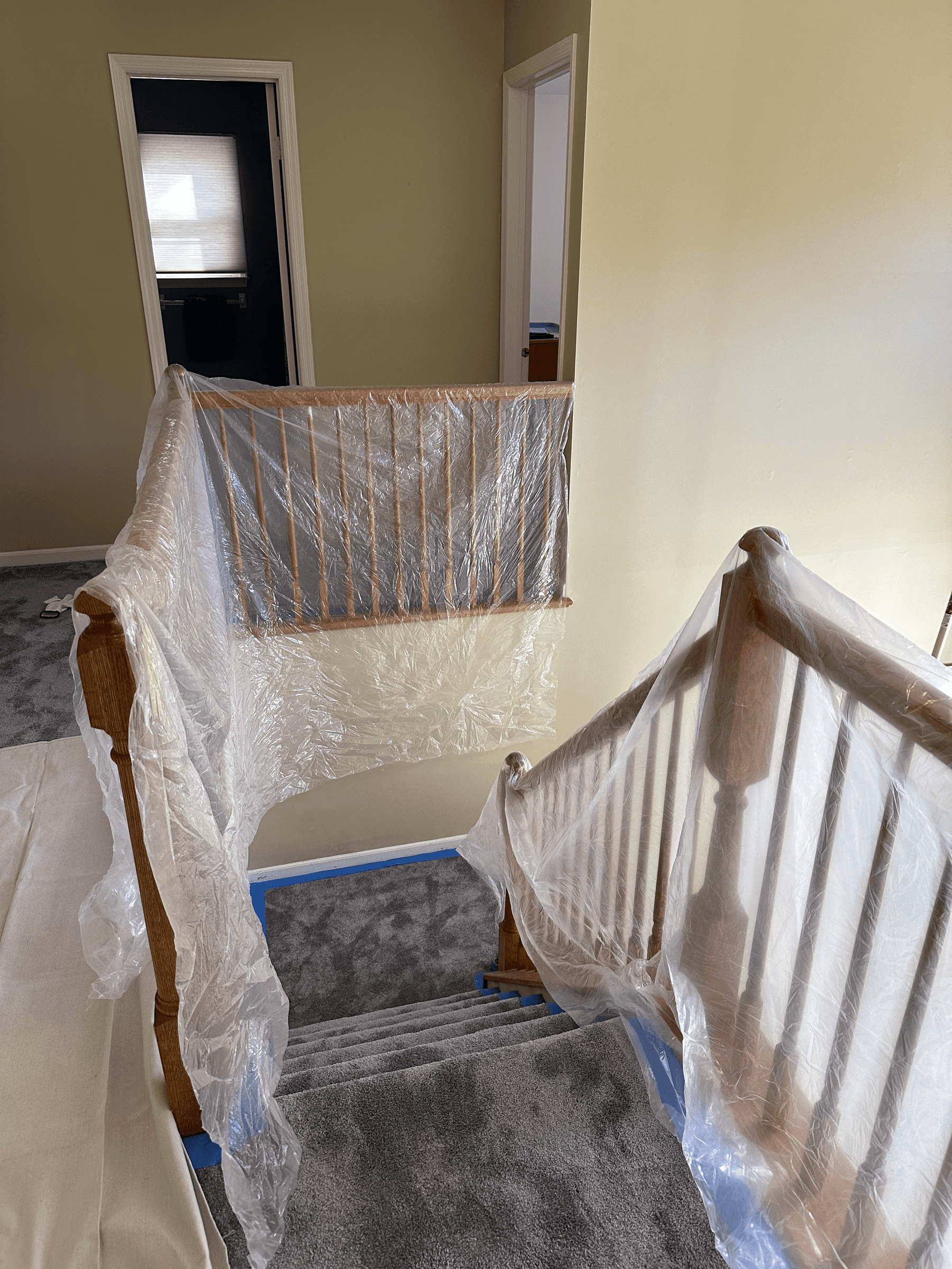 Stair railing wrapped in plastic and stair carpet covered before painting